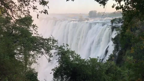 Victoria falls view through tree branches water gushing, medium shot pan Stock Footage 155644557