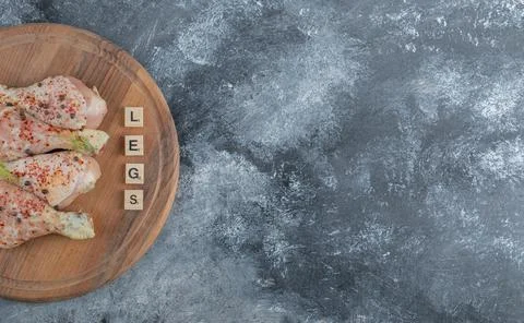 Vide angle photo of Raw chicken drumsticks with pepper on wooden board Stock Photos