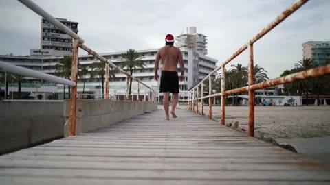 Video from the back of a bearded man with a Santa Claus hat walking over a be Video stock 140940668