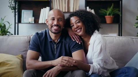 Video of beautiful couple looking at camera while sitting on the couch at hom Stock Footage 328186802