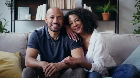 Video of beautiful couple looking at camera while sitting on the couch at hom Stock Footage 328186819