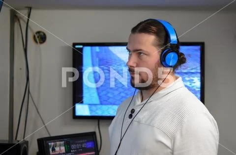 Video Broadcast Editor With Headphones Watching An Action On The Monitor. L..