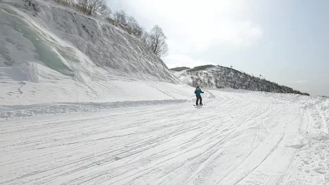 Video of camera movement on a snowy slope with ice and a cowering snowboarder Stock Footage 256799063