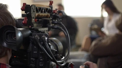 A video cameraman operates a camera with actors on a video production set. Stock Footage 99427681