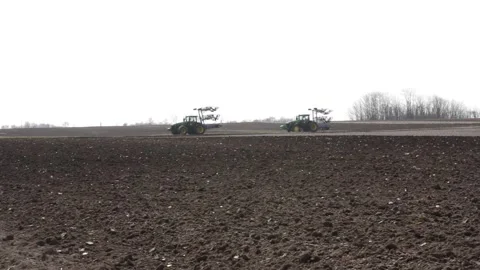 The video captures a tractor convoy moving across the horizon Stock Footage 302451219