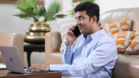 Video clip of an Indian man talking on the phone and working on his laptop. Stock Footage 229256169
