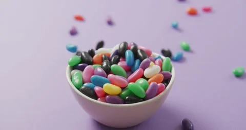 Video of close up of multi coloured sweets falling into bowl over purple Stock Footage 339160381