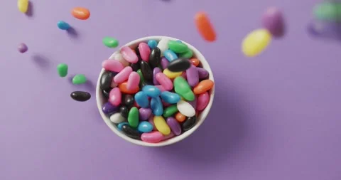 Video of close up of multi coloured sweets falling into bowl over purple Stock Footage 341664309