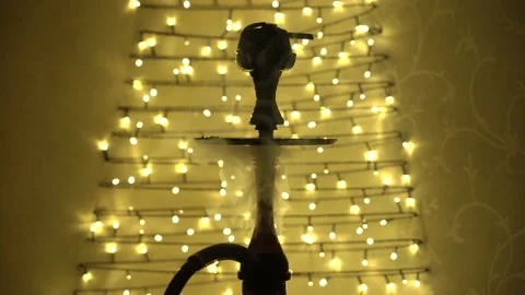 Video of close up view of hookah with blowing smoke with garlands backlight Stock Footage 163084610