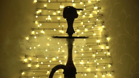 Video of close up view of hookah with blowing smoke with garlands backlight Stock Footage 163084773