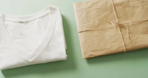 Video of close up of white folded t shirt with brown paper parcel on green Stock-Footage 331294973