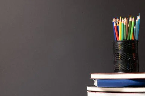 Video of composition of crayons in container on stack of books on grey 스톡 사진