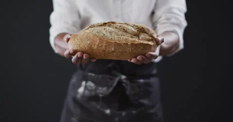 Video of cook holding loaf of bread on black background Stock Footage 339589469