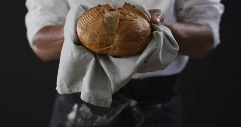 Video of cook holding loaf of bread on black background Stock Footage 341392648