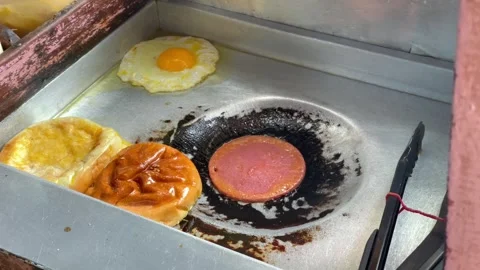 Video cooking egg, processed meat, and burger bun on a griddle Stock Footage 322588570
