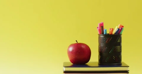 Video of crayons in container, books and apple on yellow surface Stock Footage 331294442