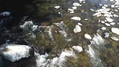 Video of a drone flying over a fast flowing, clear river with the shadow of the  Stock Footage 157455505