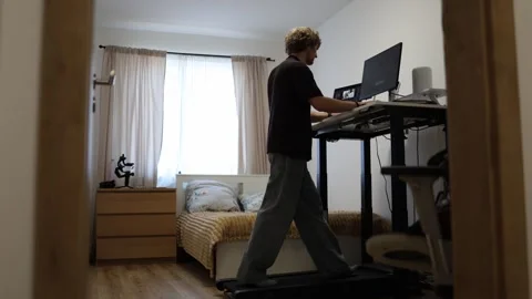 Video editor edits footage on computer while walking on treadmill at home Stock Footage 347269698