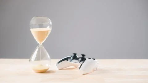 Video game controller sits beside flowing sand hourglass, hour glass shows .. Stock Photos