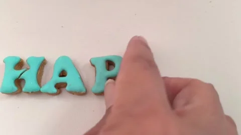 Video of hand assembling 'HAPPY' word using letter cookies with icing Stock Footage 321384736
