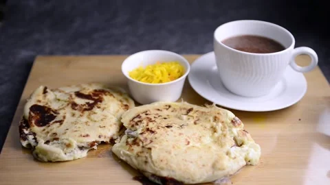 Video of a hand taking a cup of hot chocolate served with 2 pupusas and curti Stockbeeldmateriaal 221275328