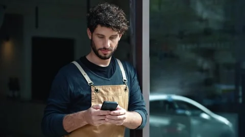 Video of handsome waiter using smartphone while leaning on the coffee shop do Stock Footage 303369704