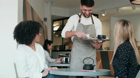 Video of handsome waitress man serving coffee and pastry for smiling women in Stock Footage 193410702
