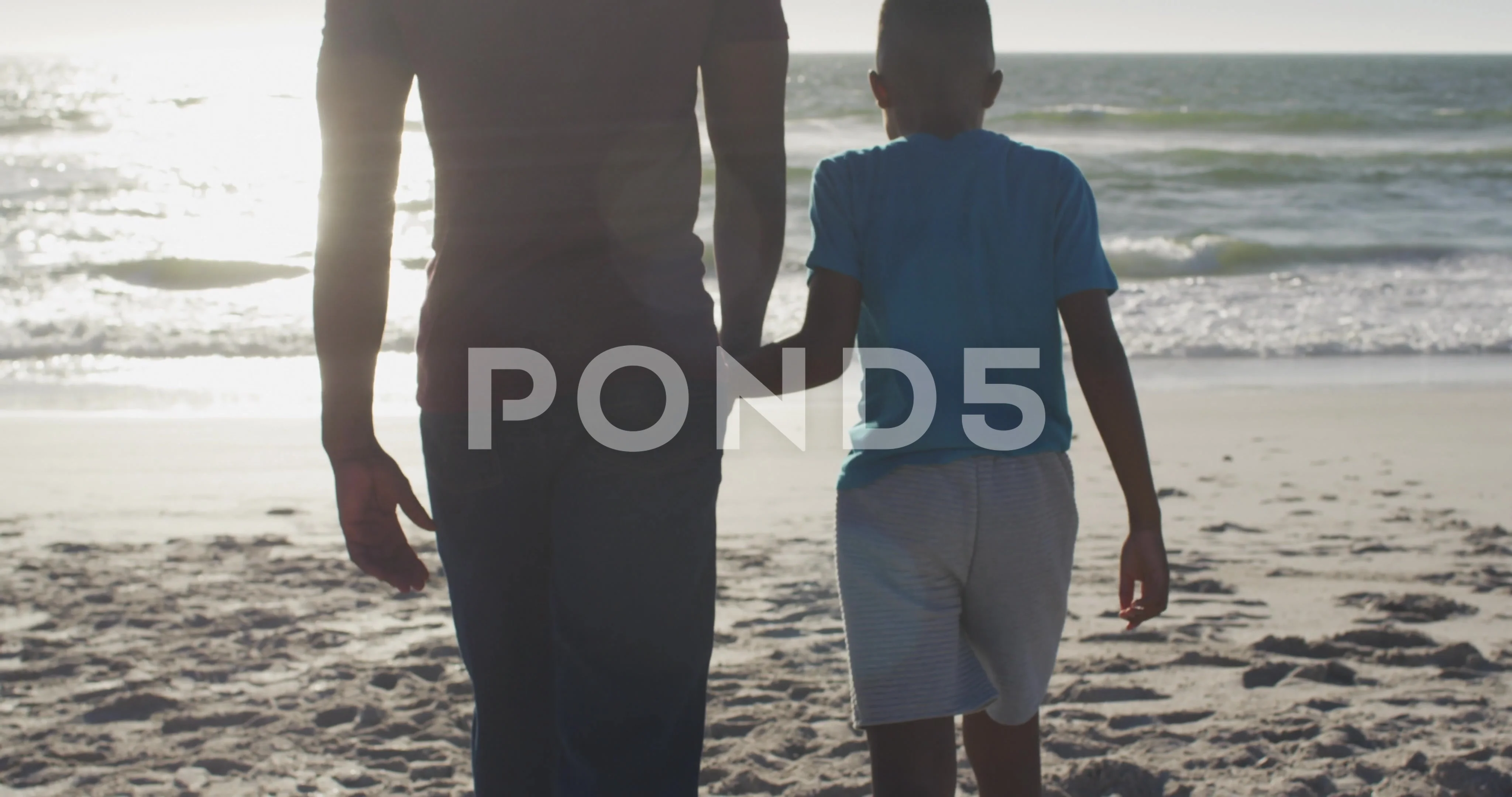 Video of happy african american father and son walking on beach at sunset