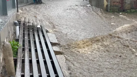 Video heavy rain causing flooding and brown water flow on urban street Stock Footage 322597238