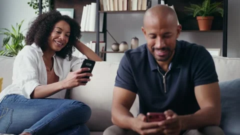 Video of lovely couple using their smartphone while sitting on couch at home. Video stock 328186551