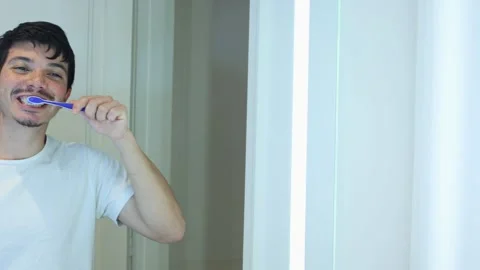 Video of a man brushing his teeth in his bathroom in front of the mirror Stock Footage 297474378