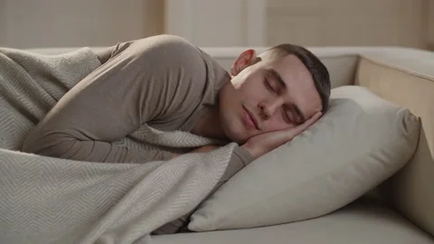 A video of a man sleeping on the couch, wrapping himself tighter in a blanket Stock Footage 234177862
