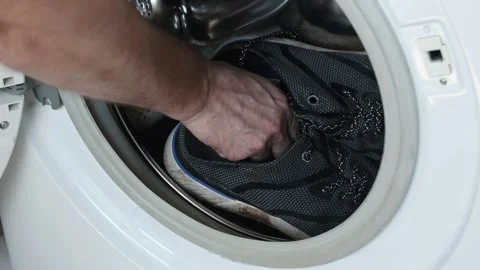 Video of a man's hand putting dirty sports shoes in the washing machine. Co.. Stock Footage 287297628