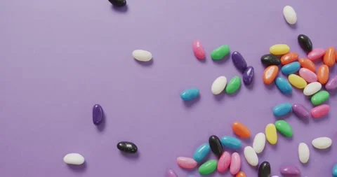 Video of overhead view of multi coloured sweets falling over purple background Stock Footage 335452844