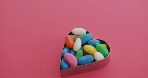 Video of overhead view of multi coloured sweets in heart shape over red Vídeo Stock 336304681