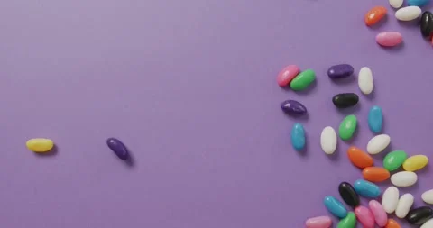 Video of overhead view of multi coloured sweets falling over purple background Stock Footage 337096209