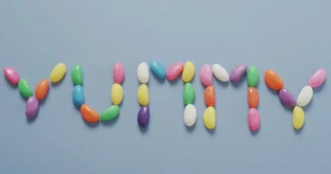 Video of overhead view of yummy text formed multi coloured sweets over blue Stock Footage 340880962