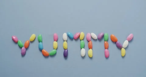 Video of overhead view of yummy text formed multi coloured sweets over blue Stock Footage 341392693