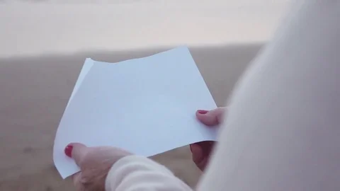 Video of paper in hands by the ocean in real slow motion Stock Footage 80663189