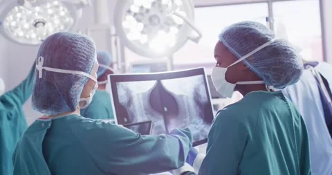 Video of rear view of two diverse female surgeons discussing x-ray in operating Stock Footage 341466821