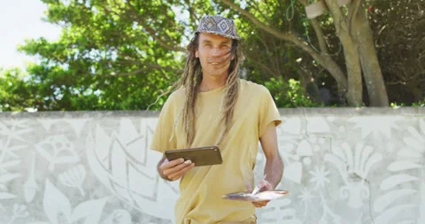 Video shows cheerful caucasian man with dreadlocks, tablet, and palette by mural Stock Footage 338324924