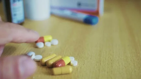The video shows a close-up of a hand sorting through a scattering of pills. Stock Footage 318384276