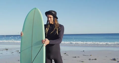 Video of smiling caucasian man with dreadlocks in wetsuit holding surfboard on Stock Footage 340971265