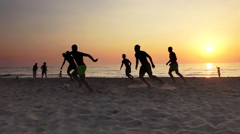 Video of a son and his father silhouette playing football on ocean beach suns Stock Footage
