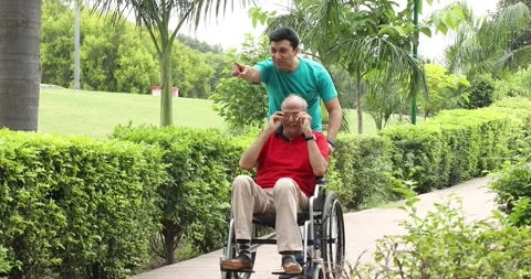 Video of son walking with disabled father in wheelchair at park. 스톡 동영상 249044648