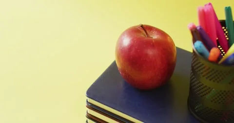 Video of stack of books, markers in container and apple on yellow background Stock Footage 331207594