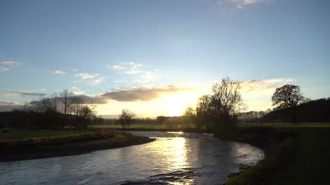 A video of the sun setting behind trees on the banks of the river Eamont on a Stock Footage 167115762