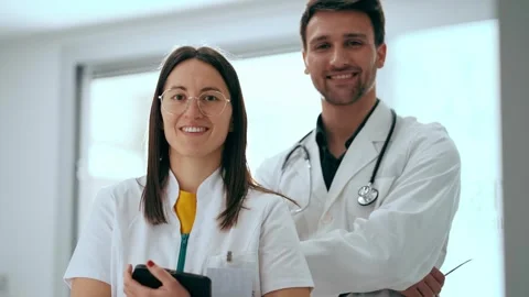 Video of of two attractive doctors smiling while looking at camera standing.. Video stock 280173967