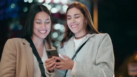 Video of two beautiful friends talking and using smartphone while walking o.. Stock Footage 235908050