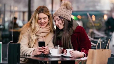 Video of two beautiful women using smartphone while drinking coffee sitting.. Stock Footage 340825304